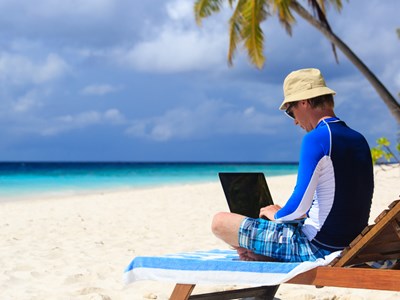 Photo of student working on laptop at the beach