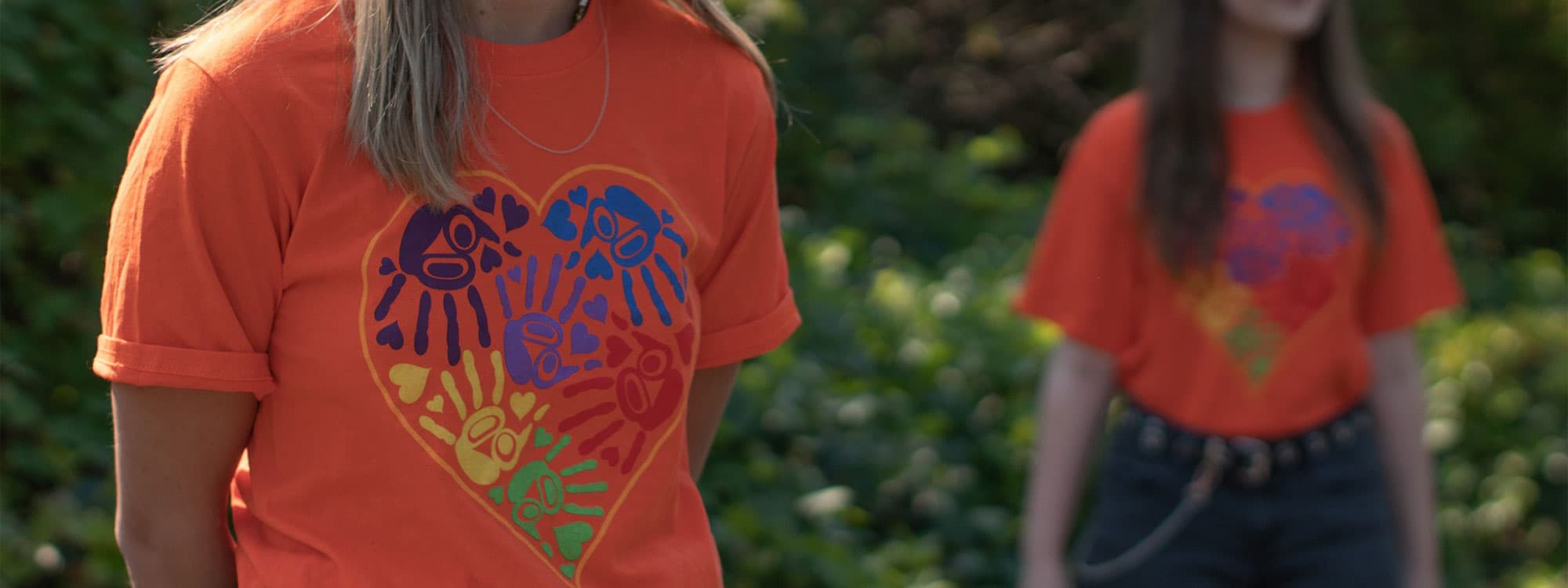 Indigenous artwork of heart with children's hands on an orange t-shirt. 