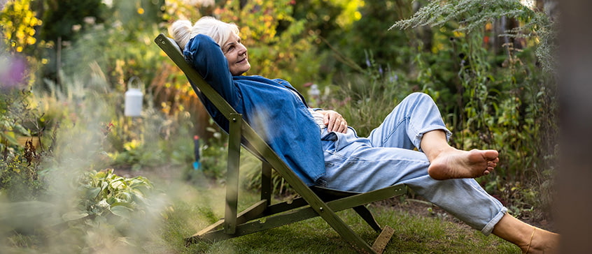 Person relaxing in a reclining chair surrounded by a lush garden, symbolizing stress-free gardening and enjoying nature in a serene outdoor setting.