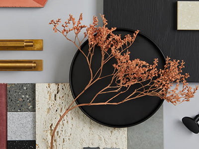 Flat lay of interior design materials including fabric swatches, stone tiles, brass handles, and a dried floral accent arranged on a neutral background, symbolizing design planning.