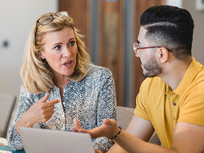 Two teachers having a conversation while working at a laptop.