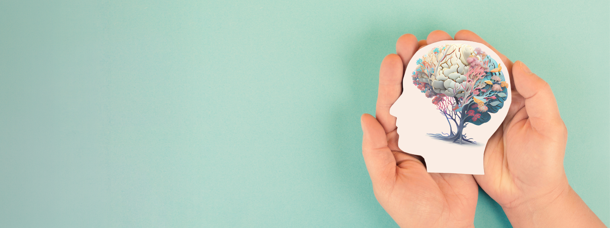 Hands gently holding a paper cutout of a human head with a colourful, tree-like brain illustration inside, set against a teal background.