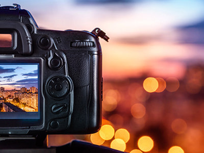 Digital camera on a tripod capturing a cityscape at sunset, with vibrant bokeh lights in the background, representing creative photography techniques.