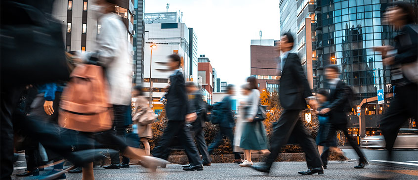 Photo of urban crosswalk with blurs of people crossing the street. 