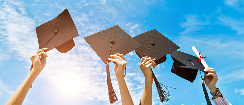 Photo of graduation caps held up against the sky.