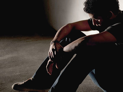 Young man sitting on ground in dark corner.