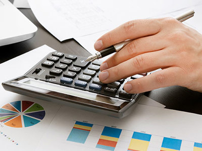 Closeup of a hand using a calculator with printed graphs in the background. 