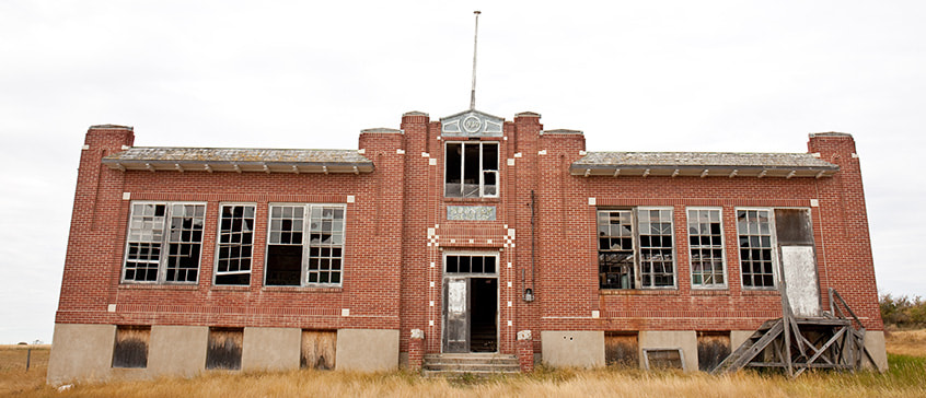 Abandoned red-brick school building with broken windows and boarded doors, representing a former residential school and the legacy of colonial policies in Canada.