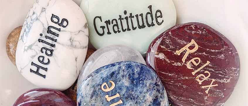 Coloured, polished stone in a pile with words and thoughts engraved on them like Gratitude, Healing and Relax.