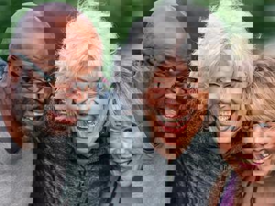 Portrait of a multi-ethnic group of senior friends at a park. The individuals are standing with arms around each others shoulders. They are smiling confidently directly at the camera. They are wearing casual athletic clothing