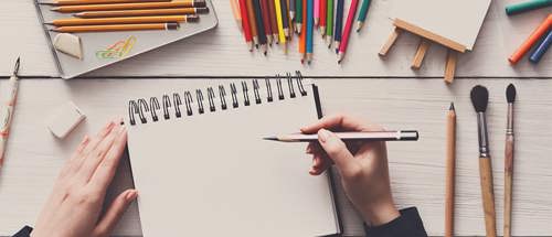 Photo of artist workstation with coloured pencils and paintbrushes.