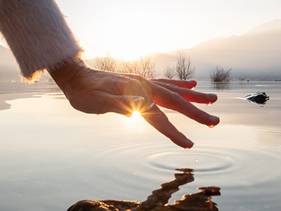 Photo of a hand skimming the surface of a lake.