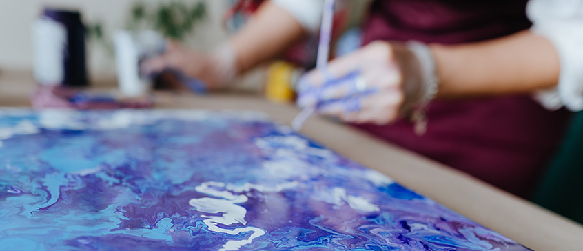 Close-up of fluid acrylic paint in vibrant purple and blue tones spreading organically across canvas, with artist