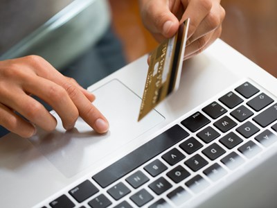 Closeup of hand at computer holding a credit card.